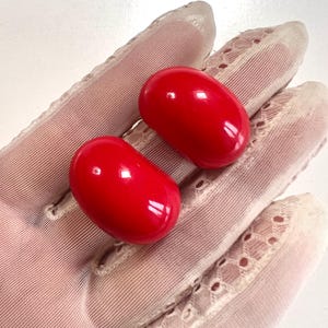 May include: A pair of red plastic clip-on earrings. The earrings are shaped like a rounded rectangle.