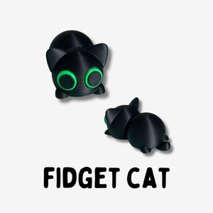 May include: Two black cat figurines with green eyes. The cat on the left is sitting up and the cat on the right is lying down. The text "FIDGET CAT" is printed below the cats.
