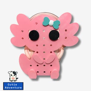 May include: Pink axolotl-shaped wall organizer with a teal bow and black eyes. The organizer has a dotted pattern and is made of a soft, flexible material.