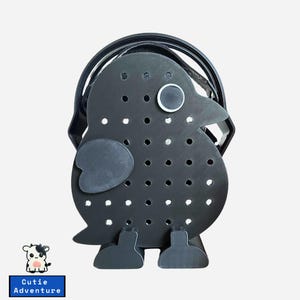 May include: Black bird-shaped tote bag with a handle. The bag has a perforated design with a large eye and a small patch on the side. The bag has two feet and a beak. The text "Cutie Adventure" is on a blue rectangle.