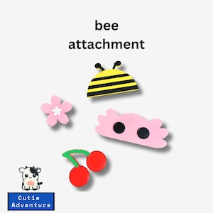 May include: A set of five colorful bee themed attachments, including a bee, a cherry, a flower, and two pink cloud shapes with black dots. The text "bee attachment" is written above the bee.