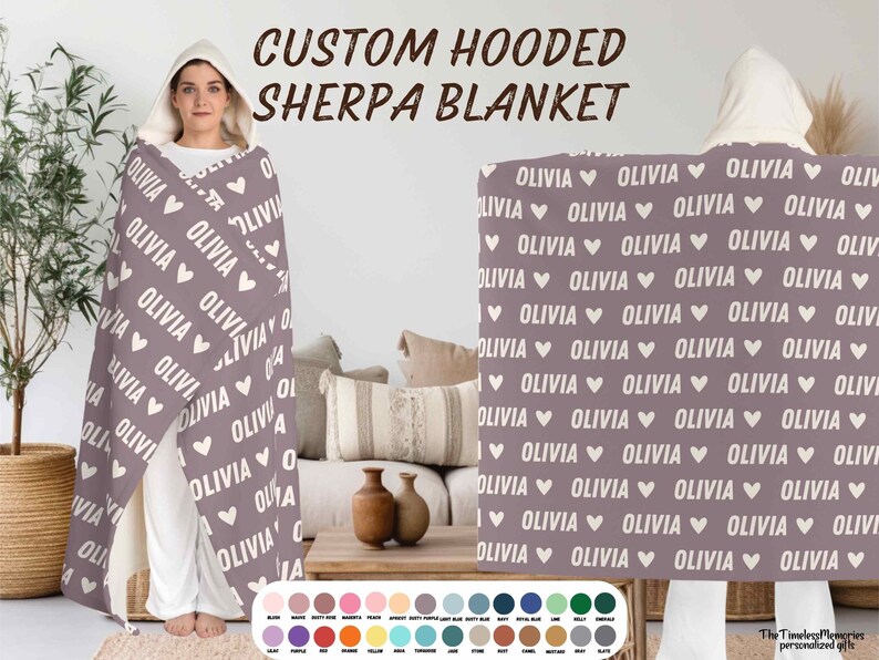 K&ouml;nnte beinhalten: Eine lilafarbene Sherpa-Decke mit Kapuze, auf der der Name "Olivia" in wei&szlig;er Schrift mit Herzen wiederholt wird. Die Decke ist &uuml;ber einer Person drapiert und flach auf einem Sofa ausgelegt.