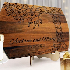 May include: Personalized wooden cutting board with a tree design, a heart carved into the tree trunk with the initials "A+M" and the text "Andrew and Mary Est. 06.25.22".