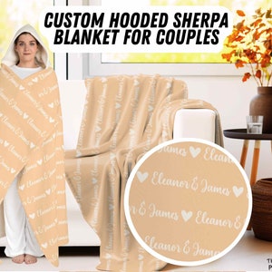 K&ouml;nnte beinhalten: Eine personalisierte Sherpa-Decke mit Kapuze f&uuml;r Paare in hellbeige mit den Namen "Eleanor & James", die sich &uuml;ber die gesamte Decke wiederholen. Die Decke ist &uuml;ber ein Sofa und einen Beistelltisch mit einer Vase mit Herbstbl&auml;ttern gelegt.
