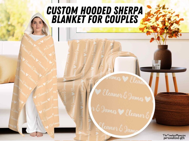 K&ouml;nnte beinhalten: Eine personalisierte Sherpa-Decke mit Kapuze f&uuml;r Paare in hellbeige mit den Namen "Eleanor & James", die sich &uuml;ber die gesamte Decke wiederholen. Die Decke ist &uuml;ber ein Sofa und einen Beistelltisch mit einer Vase mit Herbstbl&auml;ttern gelegt.