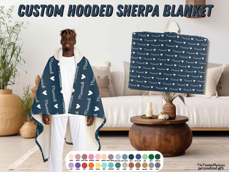 K&ouml;nnte beinhalten: Eine marineblaue Kapuzen-Sherpa-Decke mit einem wei&szlig;en Herzen und dem Namen "Maverick", der sich auf dem Stoff wiederholt. Die Decke wird von einer Person getragen. Die Decke ist in verschiedenen Farben erh&auml;ltlich.