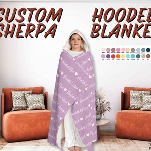 K&ouml;nnte beinhalten: Eine lilafarbene Sherpa-Decke mit Kapuze mit wei&szlig;em Text, der "Charlotte & Elijah" wiederholt &uuml;ber die gesamte Decke verteilt ist. Die Decke ist &uuml;ber einer Person drapiert, die ein wei&szlig;es Hemd und Jeans tr&auml;gt. Der Text "Custom Sherpa" und "Hooded Blanket" ist oben im Bild zu sehen.