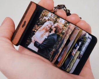 May include: A black leather photo album keychain with a wooden heart detail. The album features a photo of a couple in a wedding setting.
