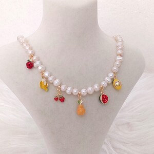 May include: A pearl necklace featuring charms shaped like various fruits: a red apple, banana, strawberries, orange, and watermelon. The necklace is displayed on a white mannequin.