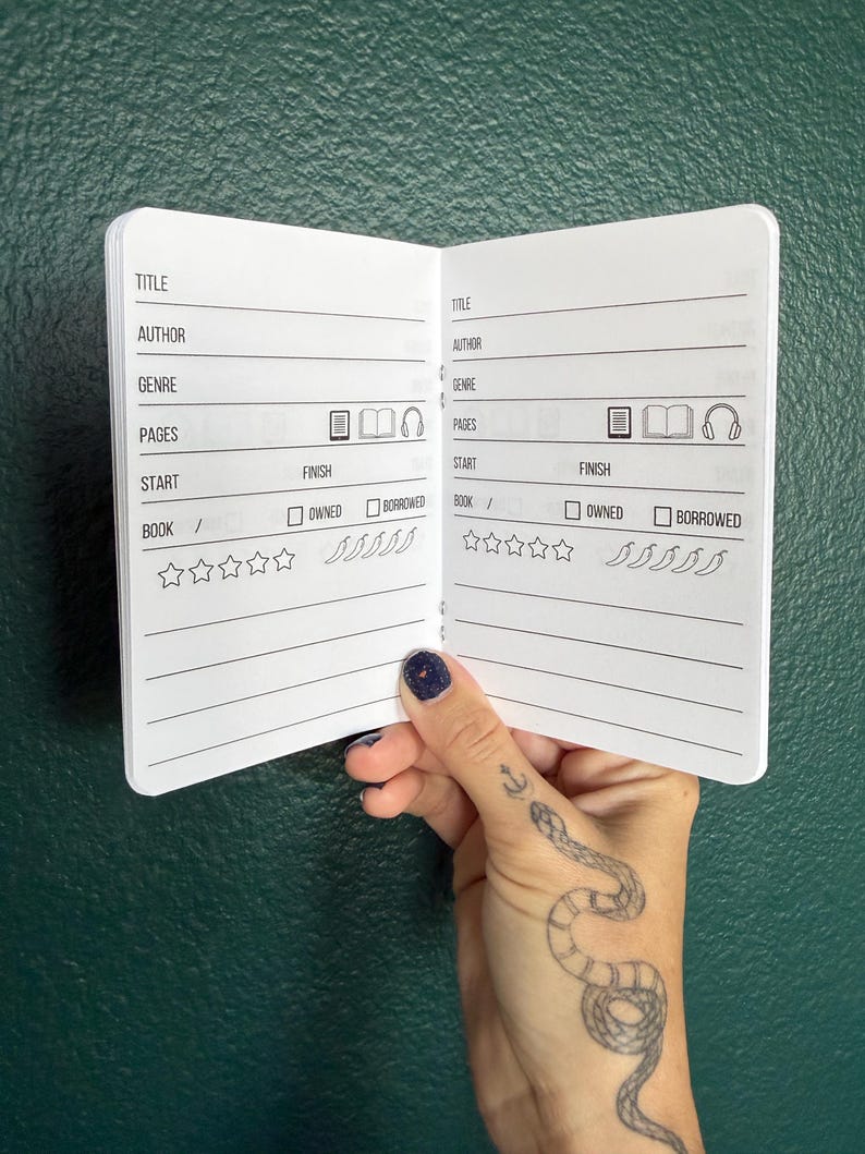 May include: A small open notebook with white pages featuring printed black text and icons for tracking reading progress. The layout includes fields for title, author, genre, pages, start and finish dates, and checkboxes for owned or borrowed status.