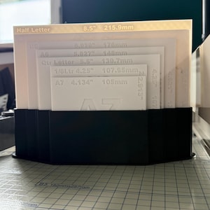 May include: A black plastic organizer stand holding a set of white paper size templates. The templates are labeled with text including Half Letter, B6, A6, Qtr Letter, 1/8Ltr, and A7, along with their specific dimensions in inches and millimeters.