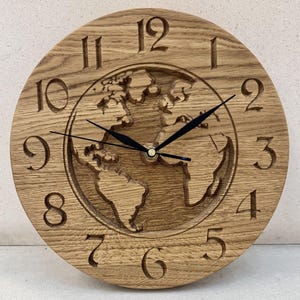 Könnte beinhalten: Eine Wanduhr aus Holz mit einem geschnitzten Globus-Design. Das Zifferblatt der Uhr hat römische Ziffern und schwarze Zeiger. Die Uhr ist aus hellbraunem Holz.