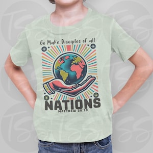 May include: A light green t-shirt featuring a colorful graphic of a hand holding a globe. The text "Go Make Disciples of all Nations" and "Matthew 28:19" are printed on the shirt. The design includes a radiant sunburst effect.