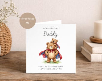 May include: A square greeting card featuring a watercolor illustration of a large brown bear wearing a red and blue superhero cape with a smaller bear on its shoulders. The text reads: TO MY AMAZING Daddy, YOU ARE MY SUPERHERO, LOVE FROM ETHAN XX.