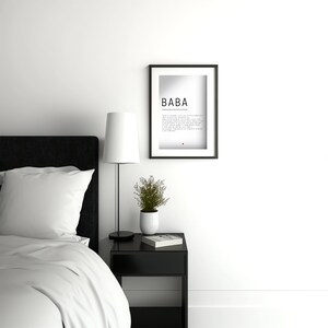 May include: A black and white framed print with the word "BABA" in bold text. The print is hanging on a white wall above a black nightstand with a white lamp and a small potted plant.