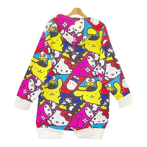 May include: A long-sleeved, hooded sweatshirt featuring a colorful pattern of cartoon characters in yellow, pink, blue, and white. The cuffs and hem are white. The sweatshirt is hanging on a wooden hanger.