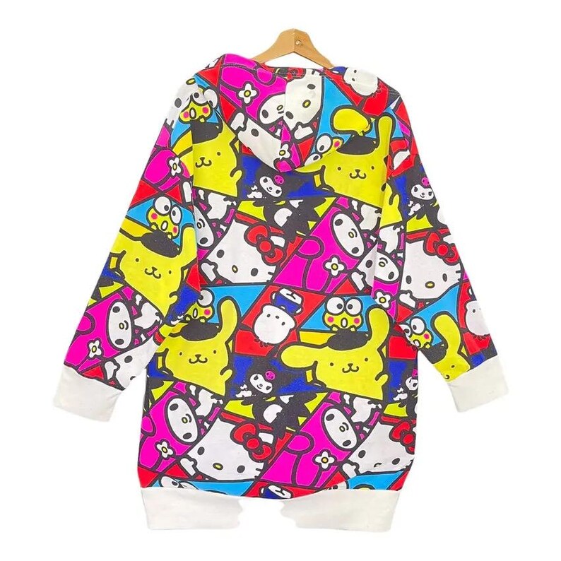 May include: A long-sleeved, hooded sweatshirt featuring a colorful pattern of cartoon characters in yellow, pink, blue, and white. The cuffs and hem are white. The sweatshirt is hanging on a wooden hanger.
