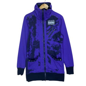 Puede incluir: Sudadera con capucha morada con cremallera y detalles negros. La chaqueta presenta diseños de salpicaduras negras, tachuelas plateadas y el texto "LET IT GO SEX PUT BAD POSTURE". Puños y dobladillo inferior negros.