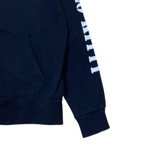 May include: Black hooded sweatshirt with a front pocket and white lettering on the sleeve. The sleeve features a ribbed cuff. The sweatshirt is made of a soft, comfortable material.