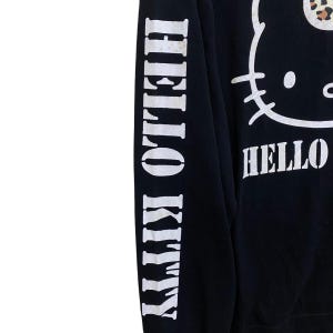 May include: Black sweatshirt featuring a white Hello Kitty graphic and the word "HELLO" in white. The left sleeve has the words "HELLO KITTY" printed vertically in white. The sweatshirt has a leopard print bow.