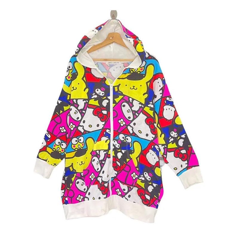 May include: A long, zip-up hoodie featuring a colorful pattern of cartoon characters in pink, yellow, blue, and white. The hoodie has a white hood lining, cuffs, and hem. The zipper is white.