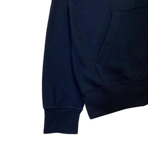 May include: Close-up of a black hooded sweatshirt. The image shows the sleeve, cuff, and pocket area of the garment. The fabric appears to be a soft, medium-weight material.