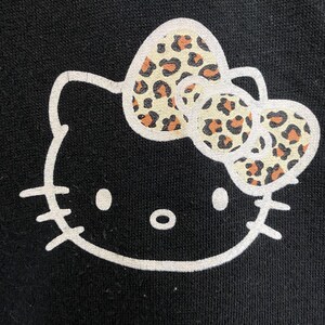 May include: Black graphic of a cartoon cat face with a white outline. The cat's bow has a tan and brown leopard print pattern. The cat has white eyes and a black nose.