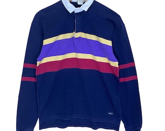 May include: Navy blue long-sleeve rugby shirt with a white collar and a three-button placket. The shirt features horizontal stripes in yellow, purple, and burgundy across the chest. The sleeves have burgundy stripes.