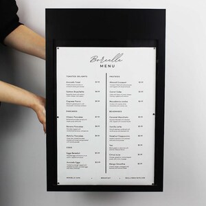 Black metal restaurant menu display box shown from the front to demonstrate its rectangular frame and printed menu insert. Wall mounted commercial menu holder for cafes, bakeries and restaurant entrance signage.