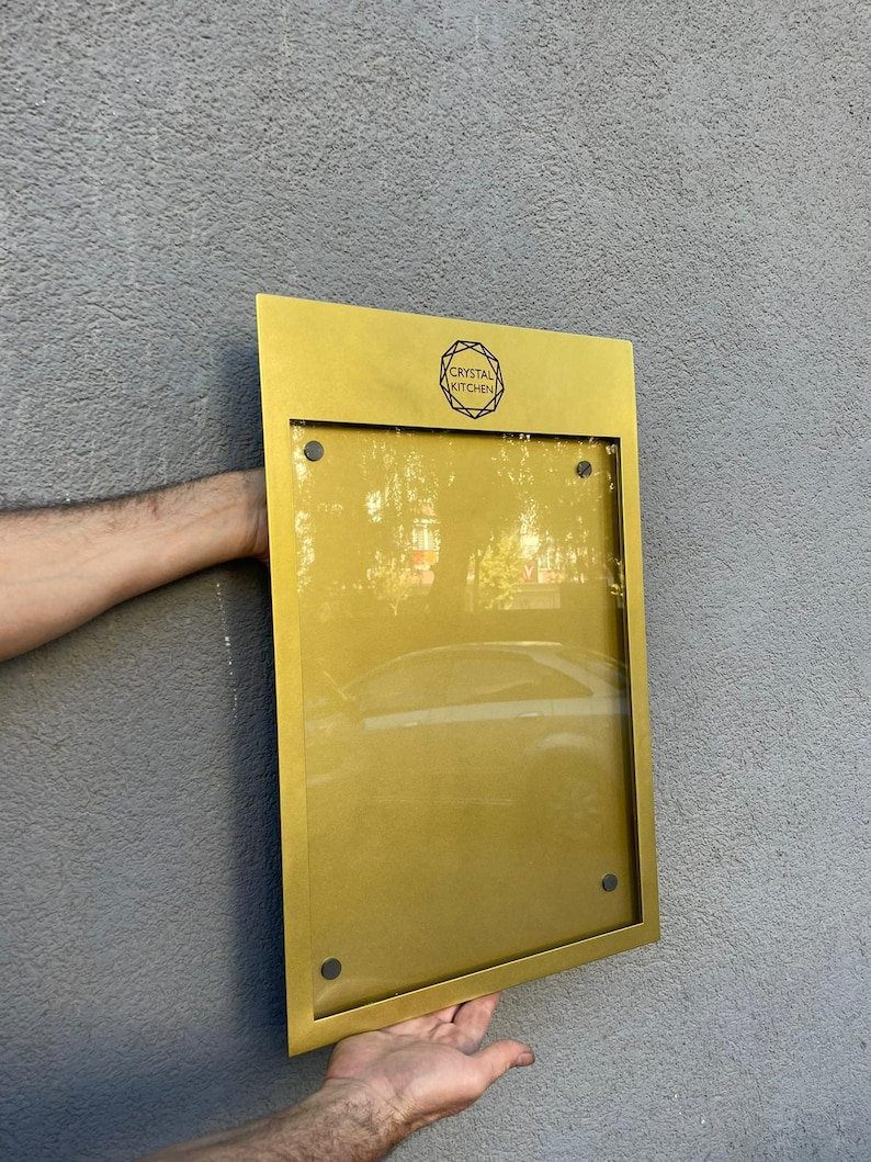 Gold metal wall menu display case with a customized upper section and transparent acrylic front. Personalized restaurant menu cabinet for premium dining venues, hotel restaurants and hospitality entrance signage.
