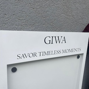 White wall mounted menu cabinet with a recessed central display area and two visible upper fasteners. Minimalist restaurant price list display for boutique hotels, dining venues, cafes and commercial interiors.