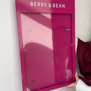 Magenta wall mounted menu display board with a glossy metal finish and clear acrylic front cover secured at four corners. Personalized restaurant signage for colorful cafe interiors, dessert bars and retail price lists.