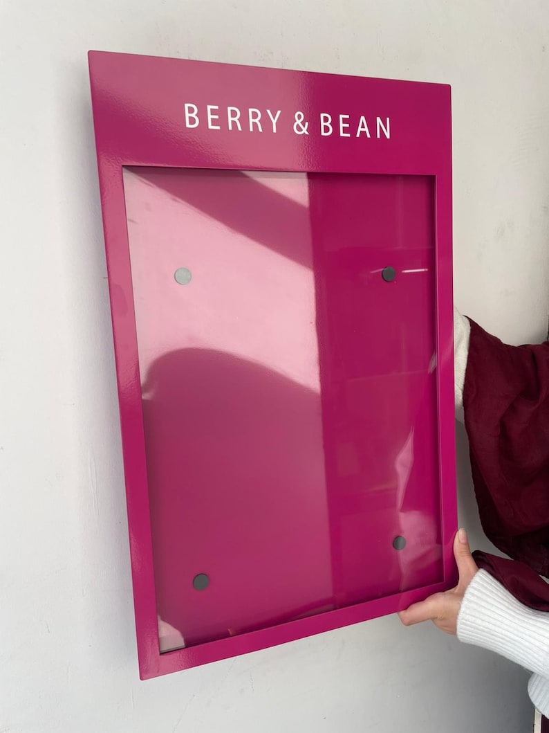 Magenta wall mounted menu display board with a glossy metal finish and clear acrylic front cover secured at four corners. Personalized restaurant signage for colorful cafe interiors, dessert bars and retail price lists.