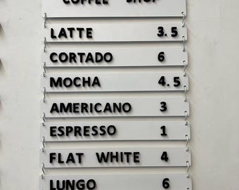 May include: A white sign with black lettering that reads "COFFEE SHOP." Below, individual lines list coffee drinks: Latte, Cortado, Mocha, Americano, Espresso, Flat White, Lungo, and Macchiato. Each drink has a corresponding number.