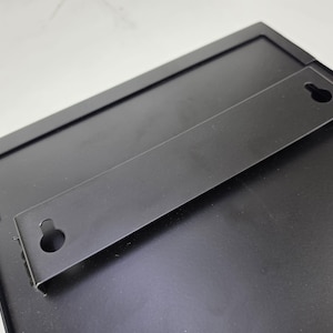 Black Wall Mounting Bracket 
Black metal rear mounting bracket with two keyhole slots for securing a restaurant menu display case to a wall. Concealed installation detail for a commercial menu cabinet and wall mounted signage system.