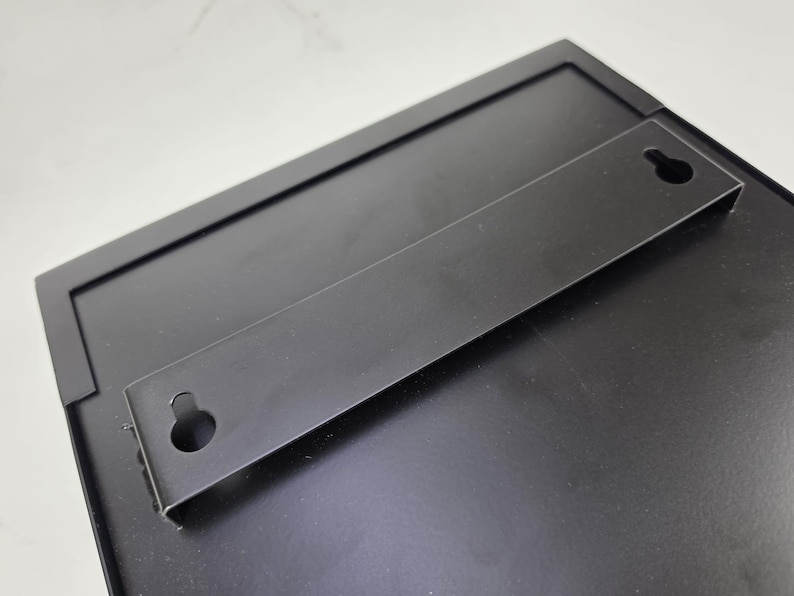 Black Wall Mounting Bracket 
Black metal rear mounting bracket with two keyhole slots for securing a restaurant menu display case to a wall. Concealed installation detail for a commercial menu cabinet and wall mounted signage system.
