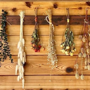 Peut inclure: Un mur en bois avec dix bouquets de fleurs s&eacute;ch&eacute;es et de verdure suspendus &agrave; un support en bois. Les bouquets comprennent de la lavande s&eacute;ch&eacute;e, de l'eucalyptus, des fleurs blanches et duveteuses, de petites fleurs orange, des fleurs blanches, des fleurs jaunes, des pommes de pin brunes et des fleurs violettes.