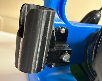 May include: A close-up of a black plastic holder attached to a blue plastic surface. The holder has a cylindrical shape and is designed to hold a small object, such as a tool or a pen.