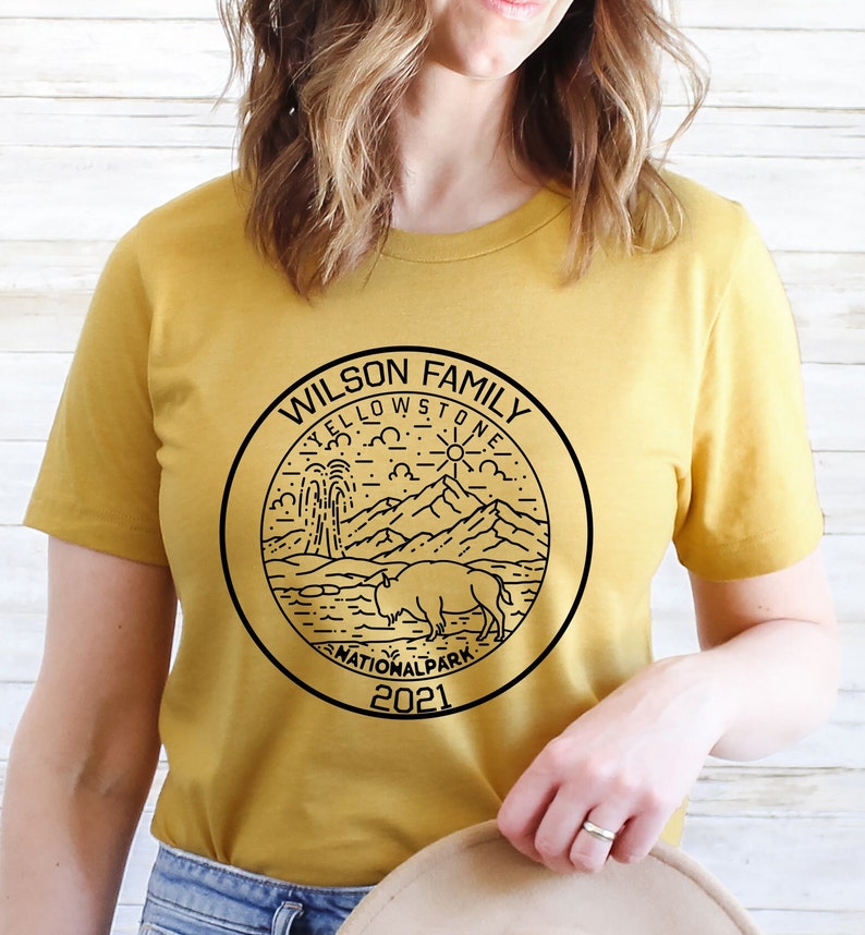 May include: A mustard yellow t-shirt with a black graphic of a Yellowstone National Park logo. The logo features a mountain range, a geyser, a bison, and the text "Wilson Family Yellowstone National Park 2021".