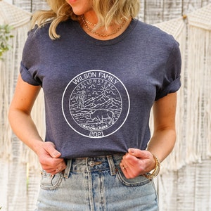 May include: A navy blue t-shirt with a white graphic design of a Yellowstone National Park logo. The logo features a bison, mountains, a sun, and the text "Wilson Family Yellowstone National Park 2021".