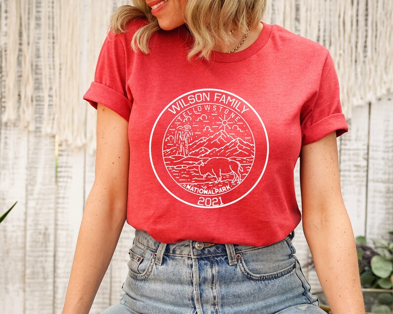 May include: Red t-shirt with a white graphic of a Yellowstone National Park logo. The logo includes a bison, mountains, a geyser, and the text "Wilson Family Yellowstone National Park 2021".