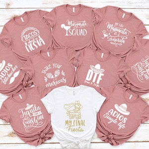 Op de afbeelding: Een set van tien roze t-shirts met witte tekst en afbeeldingen. De shirts bevatten verschillende zinnen die te maken hebben met een fiesta, waaronder "Tacos about a Fiesta", "Margarita Squad", "My Last Mamacita as a Señorita", "Shake Your Maracas", "DTF (Dream to Fiesta)", "Tequila and Sunshine", "Adios Bitchachos", "Tequila and Sunshine", "Adios Single Life", and "My Final Fiesta".