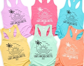 May include: Six colorful racerback tank tops. Each top features a black graphic of a sunset, palm tree, and the text "LISA'S BACHELORETTE 2022". The tops are in shades of pink, yellow, blue, and orange.