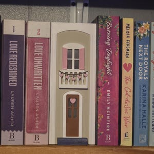 May include: A handmade wooden sign with the text "Welcome" in a whimsical font. The sign is painted white with a distressed finish, and features a decorative floral design in shades of pink and green. It is designed for indoor or outdoor use.