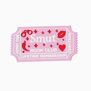 以下が含まれることがあります： 「Smut Book Club Lifetime Membership」の文字が入ったピンク色のチケット。手錠、唐辛子、唇、ハート、星の赤いグラフィックが特徴です。チケットにはギザギザの縁があり、番号は00524832です。