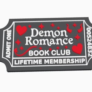 May include: A rectangular ticket-shaped plaque in black with white borders and text reading "ADMIT ONE", "Demon Romance BOOK CLUB", and "LIFETIME MEMBERSHIP". The design includes red hearts, small red stars, and red devil horns with a tail.