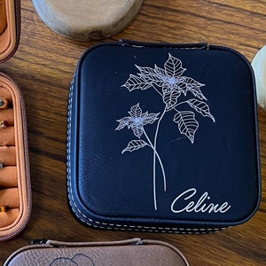 May include: Three brown leather jewellery boxes with different floral designs and personalised names. The boxes are on a wooden surface. The names on the boxes are "Peace", "Celine", and "Selena".