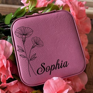 May include: A pink faux leather jewellery box with a floral design and the name "Sophia" engraved on the front.