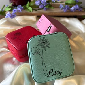 May include: Three small square jewellery boxes with zips. The boxes are red, pink and light blue. The light blue box has a floral design and the name "Lucy" engraved on it.