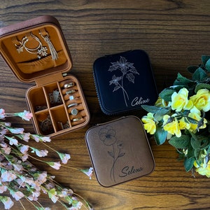 May include: Two brown faux leather jewellery boxes with floral designs and personalised names. The box on the left is open and shows compartments for rings, earrings, and necklaces. The box on the right has the name "Selena" engraved on it. The box in the middle has the name "Celine" engraved on it.